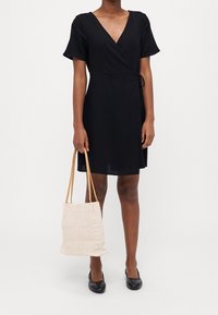 Sort omslagskjole med korte ærmer, lavet af letvægtsstof, kombineret med en beige textured tote taske og sorte flade sko.