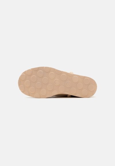 Semelle de chaussure beige clair avec de grandes accroches circulaires espacées uniformément, présentée à plat sur fond blanc.