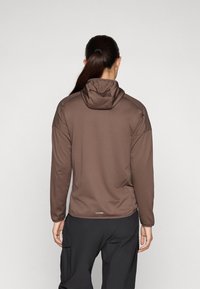Giacca cappuccio marrone con una finitura testurizzata, maniche lunghe e una vestibilità rilassata. La vista posteriore mostra un design semplice con un branding discreto all'orlo.