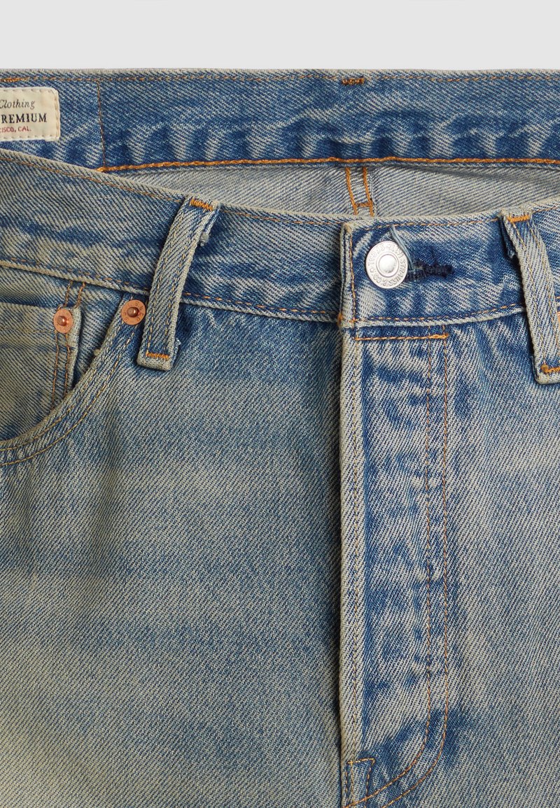 Hellblaue Jeans mit hoher Taille, Kupferknöpfen und orangefarbenen Nähten. Verfügt über zwei Vordertaschen und ein Etikett im Bund.