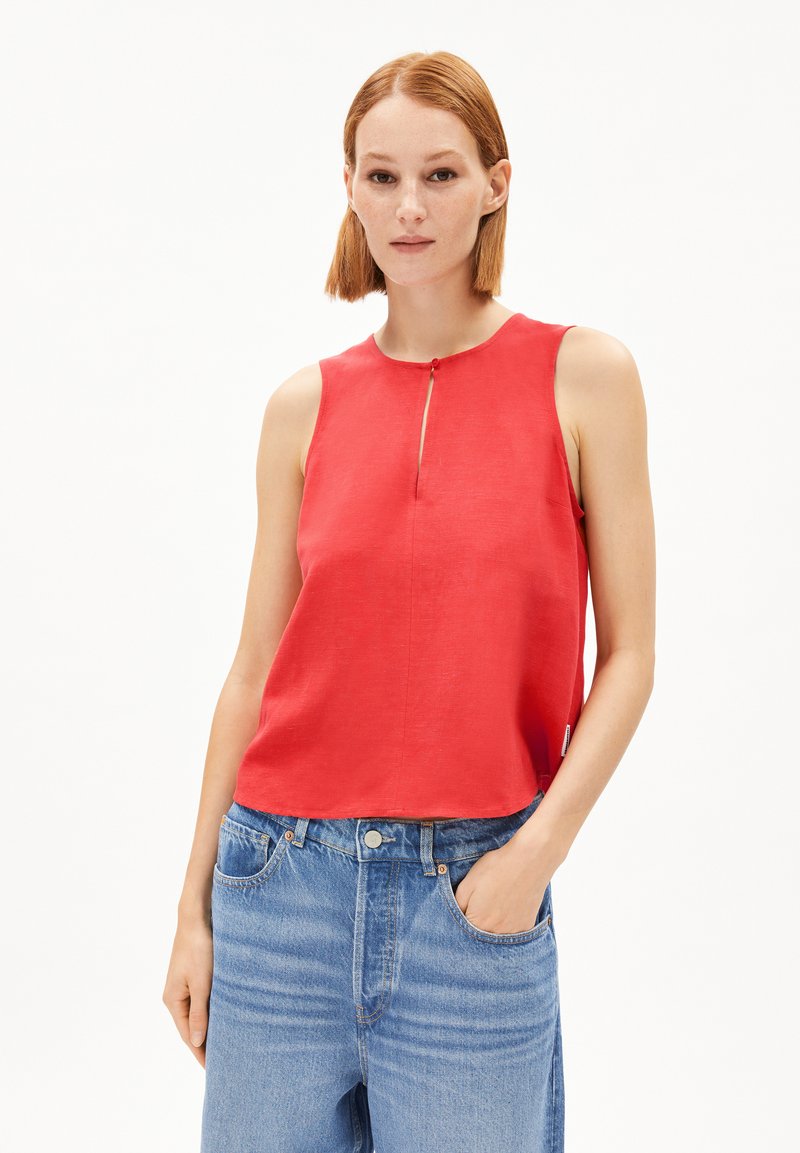 Haut sans manches rouge avec un col rond et une petite ouverture à l'avant dotée d'un bouton. Texture douce, assorti avec un jean bleu clair.