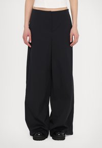 Wide-leg black trousers made of smooth fabric, featuring a tailored design with a pronounced front crease and side pockets.