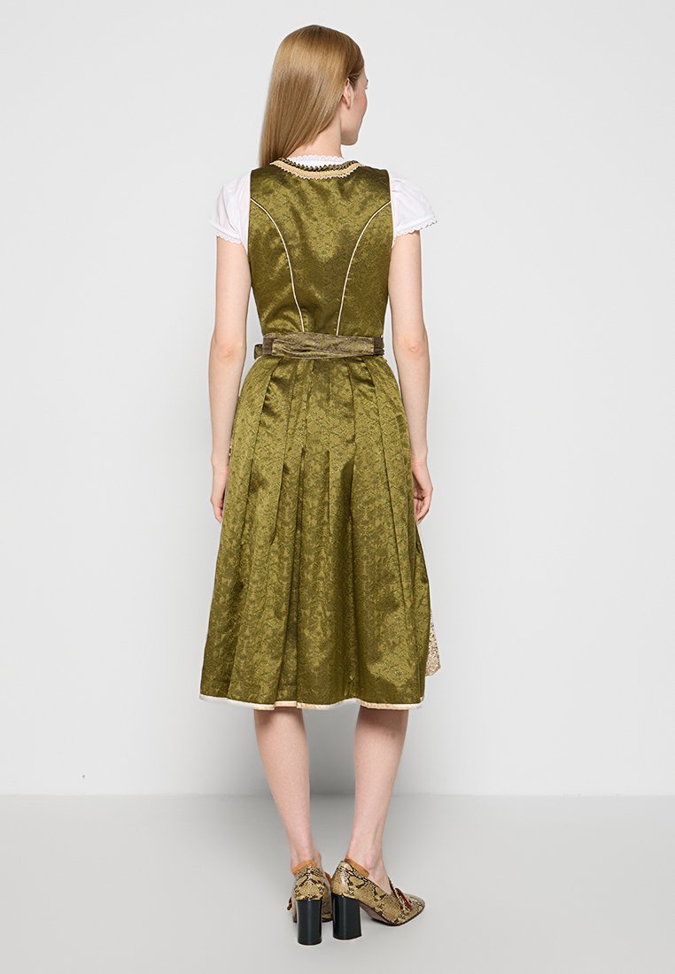 Olivegrünes Kleid mit tailliertem Oberteil und plissiertem Rock. Strukturierter Stoff und ein dekorativer Gürtel in der Taille. Weiches weißes Hemd darunter.