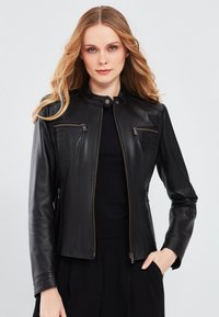 Black leather jacket with a stand collar, zippered front, and two breast pockets. Features fitted design and smooth texture.