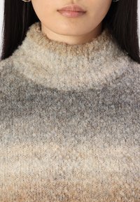 Maglione a maglia con colletto alto a coste e una sfumatura dal beige al grigio. La texture è morbida e presenta una qualità fuzzy simile al bouclé.