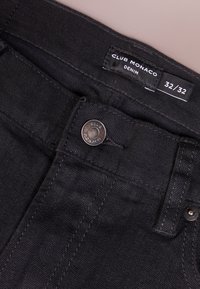 Svart denimjeans med midjeband, metallknapp och etikett som visar Club Monaco-märket och storlek 32/32.