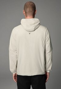 Light beige hooded jacket with long sleeves, a smooth texture, and adjustable drawstring feature. Minimalist design without external pockets.