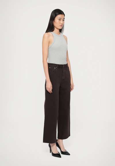 Szürke ujjatlan felső, amelyet magasderekú, bőszárú sötétbarna farmerral és fekete hegyes orrú magassarkúval párosítottak. Sima anyagú, testhez simuló fazon.