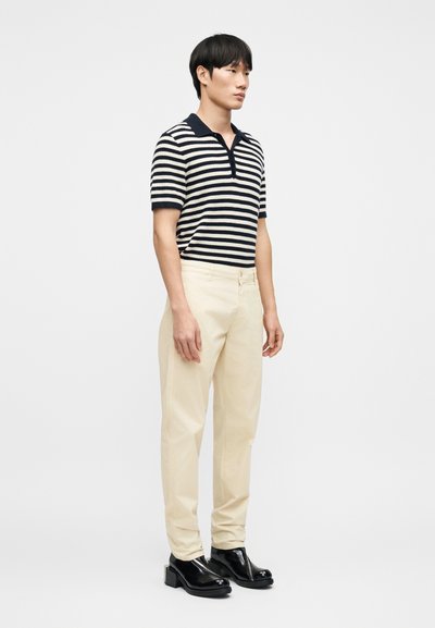 Polo rayé bleu marine et crème, pantalon beige et chaussures noires brillantes. Coupe slim, manches courtes et col.