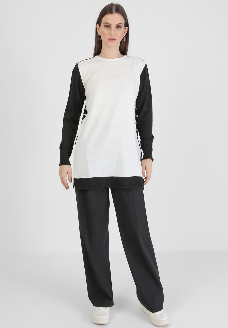 Maglietta a maniche lunghe bianca e nera con corpo bianco testurizzato e maniche nere solide, con aperture laterali e orlo dritto. Abbinata a pantaloni neri a gamba larga.