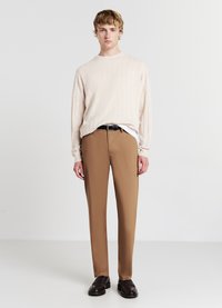 Maglione beige a coste e pantaloni marroni a gamba affusolata, abbinati a scarpe scure. Le texture morbide e il taglio classico creano una silhouette rilassata.