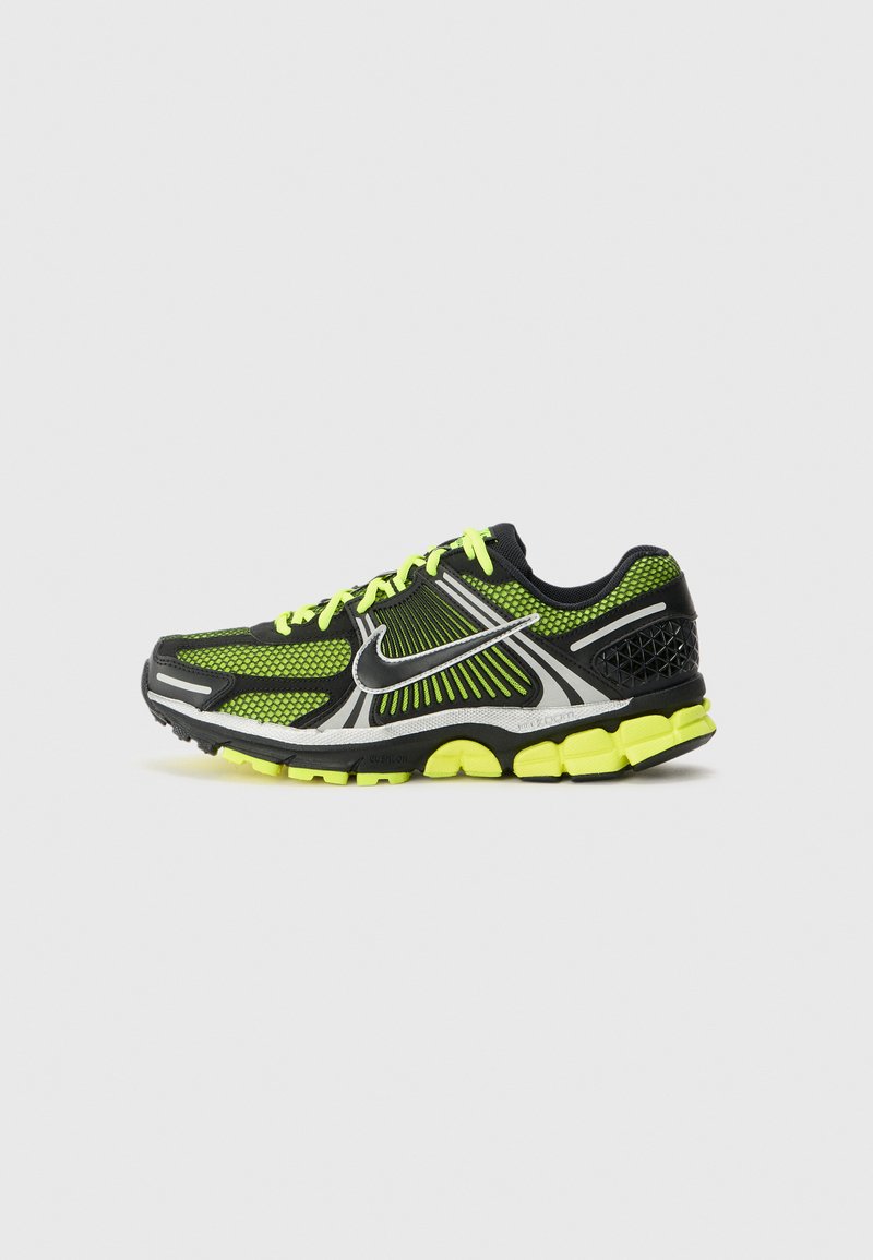 Zapatilla de running negra y verde neón con parte superior de malla, acentos plateados reflectantes y suela acolchada. Presenta un cordón llamativo y detalles texturizados.