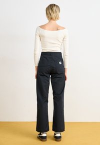 Black wide-leg pants with a high waist, textured fabric, and a back pocket. Worn with a fitted off-white top and black platform shoes.