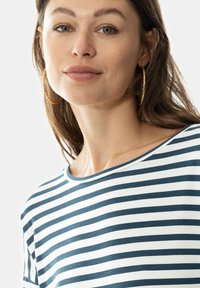 Top a righe con strisce orizzontali blu navy e bianche, scollo rotondo e vestibilità rilassata. Il modello indossa grandi orecchini a cerchio.