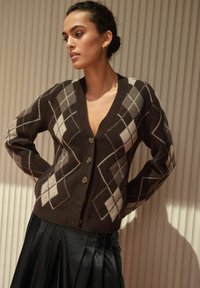 Brown argyle cardigan with a deep V-neck, featuring a button front and contrasting beige and gray diamond patterns. Soft knit texture.