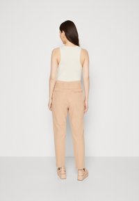 Beige Baumwollhosen mit lockerem Schnitt, mittlere Leibhöhe, mit Gesäßtaschen, kombiniert mit einem hellen ärmellosen Oberteil.