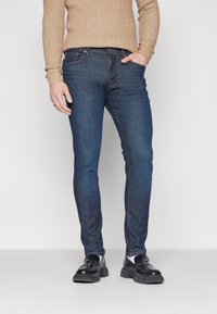 Mörkbla slim-fit jeans i denim, med en klassisk femficksdesign, sydda detaljer och knappstängning vid midjan.