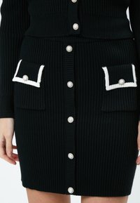 Robe en maille côtelée noire avec des boutons en perles, des accents de poche blanche et deux poches avant. Présente un design ajusté et un tissu texturé.