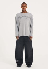 Gray ribbed long-sleeve shirt with a graphic logo, paired with loose black denim pants and black shoes. Simple, casual design.