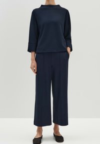 Parte superior azul marino y pantalones de pierna ancha hechos de tela suave. La parte superior cuenta con un cuello alto y mangas tres cuartos. Los pantalones tienen costuras frontales y bolsillos.