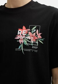 Juodas medvilnės marškinėliai su gėlių grafika rožinės ir žalios spalvos, su tekstu "PERDIZAINUOTA GAMTA ATEITYJE" ir "2007".