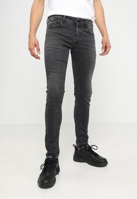 Jeans negros ajustados con un leve desvanecimiento, diseño de cinco bolsillos, detalles de costura sutiles y textura desgastada en las rodillas. Combinados con zapatillas negras.