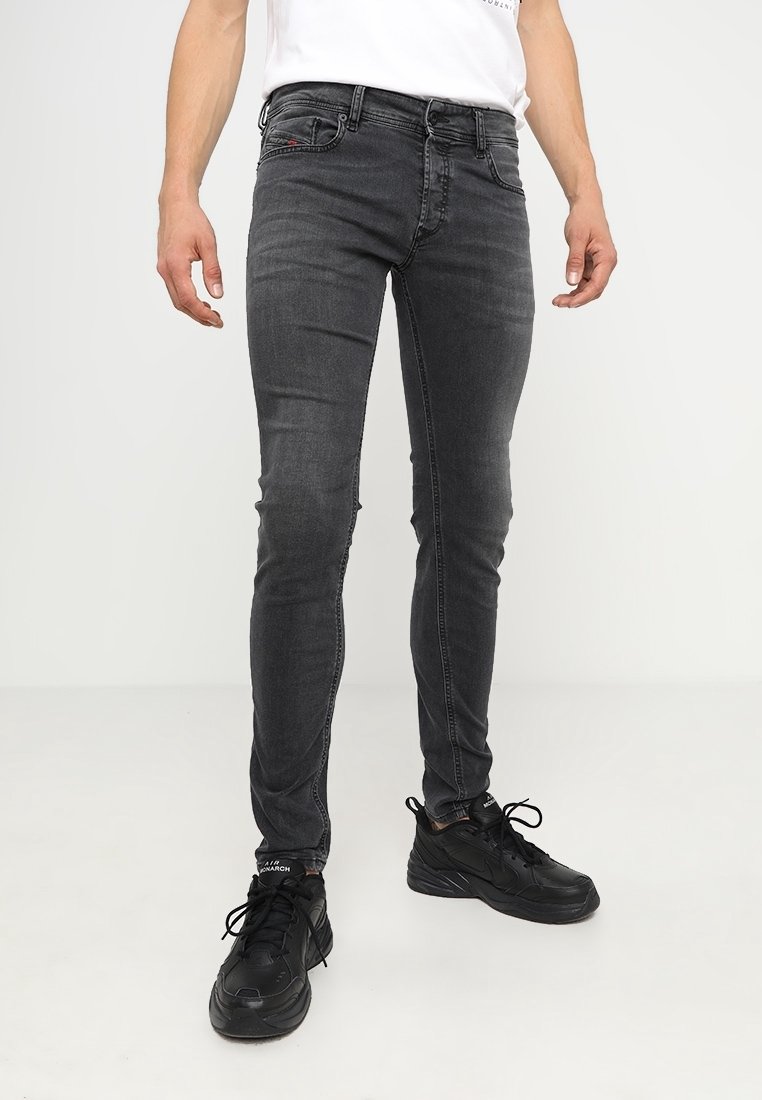 Jeans negros ajustados con un leve desvanecimiento, diseño de cinco bolsillos, detalles de costura sutiles y textura desgastada en las rodillas. Combinados con zapatillas negras.