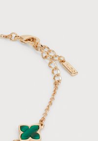 Pulsera en tono dorado con un cierre tipo langosta, que presenta un charm de flor de resina verde, acentuado por una pequeña etiqueta grabada con "ALDO".