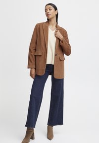 Brown corduroy blazer, cream V-neck sweater, dark denim wide-leg pants, beige ankle boots; structured fit, two front pockets, clean lines.