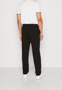 Svarta byxor med rak skärning, med en slät textur, två bakfickor och midjeband, i kombination med vita sneakers och en vit pikétröja.