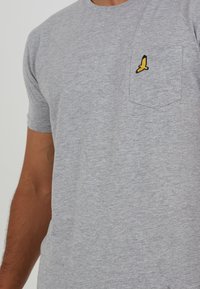 Gray short-sleeve t-shirt made of soft cotton blend. Features a yellow and black embroidered bird on the chest pocket.