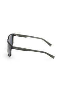 Zielone plastikowe okulary przeciwsłoneczne z ciemnymi soczewkami, charakteryzujące się eleganckim wzornictwem i prostymi zausznikami. Logo "Timberland" na zewnętrznym zauszniku.