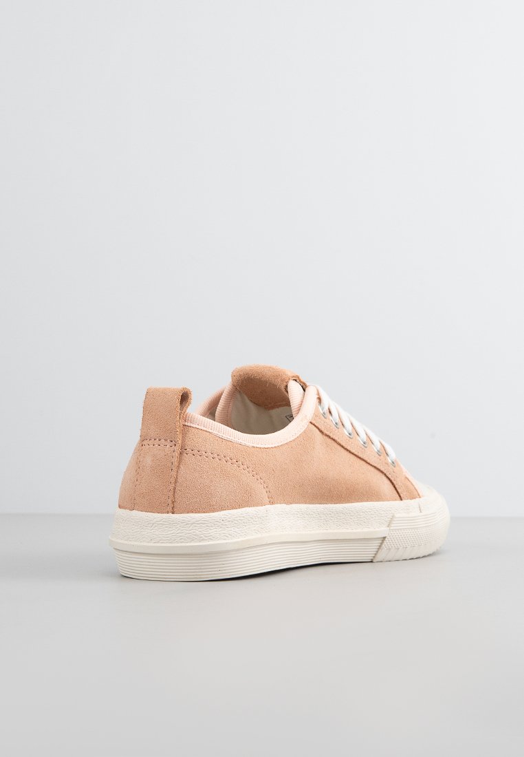 Zapatilla baja de ante melocotón con cordones blancos y suela blanca de goma gruesa, mostrada desde la parte trasera sobre una superficie y fondo neutros.