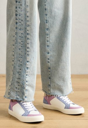 Sneakers met een witte basis, paarse en roze suède accenten, en witte veters; gecombineerd met lichtblauwe, uitgerafelde denim jeans.
