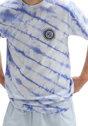Person wearing a white and blue tie-dye Vans t-shirt with a black sun logo on the chest, paired with light blue shorts.