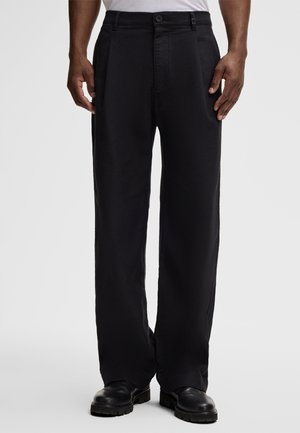 Black, wide-leg trousers with a smooth texture, pleated front, belt loops, and side pockets, paired with black chunky-soled shoes.