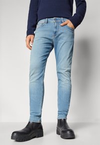 Világoskék, slim-fit farmernadrág, elülső zsebekkel és cipzáros záródással, fekete, vastag talpú csizmával párosítva.