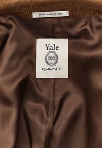 Doublure de veste en satin marron avec une étiquette de marque Yale GANT et une étiquette en tissu indiquant "Fabric Made in Italy" près du col.