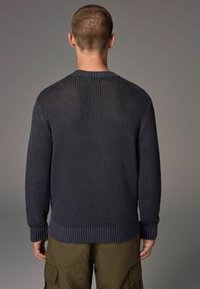 Dunkelblauer, gestrickter Pullover mit einem strukturierten Wabenmuster. Mit gerippten Bündchen und Saum. Getragen mit olivfarbenen Cargo-Hosen.
