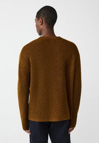Brauner gerippter Strickpullover mit Rundhalsausschnitt, überschnittenen Schultern und einer lockeren Passform; strukturierte Oberfläche und seitliche Schlitze am Saum.