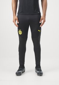 Zwarte sportbroek met een aansluitend ontwerp, voorzien van het gele Borussia Dortmund-logo en Puma-branding, aangevuld met een gestructureerde stof en details.