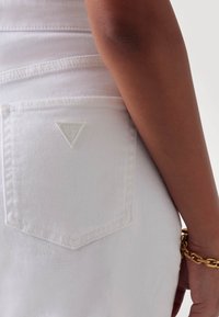 Witte denimjeans hebben een driehoekige zak met reliëfbranding. De textuur is glad, met contrasterende stiksels zichtbaar langs de naden.