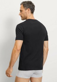 T-shirt nero a maniche corte in morbido cotone, con scollatura rotonda, design aderente e texture liscia. La vista posteriore mostra uno stile semplice.