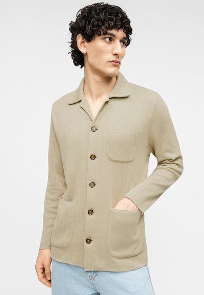 Μπεζ πλεκτή ζακέτα με απαλό φινίρισμα, που διαθέτει γιακά, επτά κουμπιά, δύο μπροστινές τσέπες και ριμπ λεπτομέρειες.