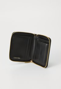 Zwarte leren Calvin Klein portemonnee met een gouden rits, meerdere kaartsleeves en een muntvak, open tegen een egale witte achtergrond.