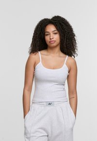 Light gray, fitted tank top with thin straps and a round neckline. Soft texture, paired with loose light gray sweatpants featuring a waistband label.