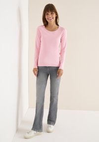 Rosa Langarmshirt mit rundem Halsausschnitt, kombiniert mit grauen Schlagjeans und weißen Sneakern. Glattes Material mit einer figurbetonten Silhouette.