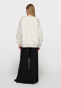 Sudadera de gran tamaño en gris claro con hombros caídos y puños acanalados, combinada con pantalones de pierna ancha en negro. Textura suave y lisa.