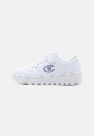 Baskets blanches avec une tige lisse imitation cuir, ornées d'un logo en strass violet, semelle plate et bride ajustable avec des accents en lacets.