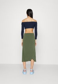 Off-shoulder marinblå crop top, olivgrön insvept kjol och blå plattformssandaler. Slät tyg med en åtsittande design och långa ärmar.
